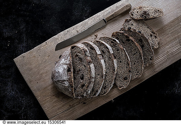 A loaf of fresh sliced brown bread on a bread board and a sharp knife