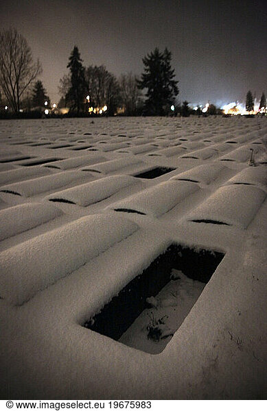 A lone  empty cemetery plot in snow in Washington at night.