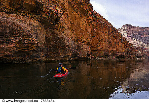 A lone kayaker paddling along a canyon wall in the Grand Canyon