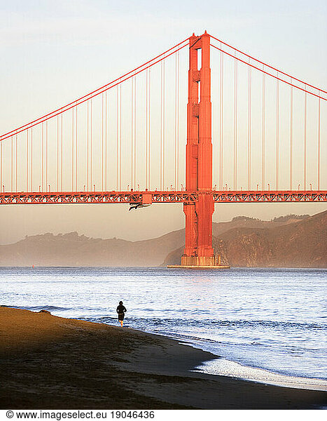 A lone person running along the bay at the Presidio with the San Francisco Golden Gate Bridge in the background.