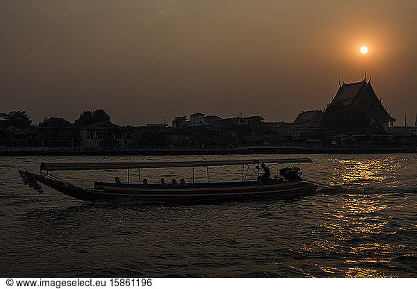 A long tail boat cruising along the Chao Phraya River during sunset time  Bangkok  Thailand.