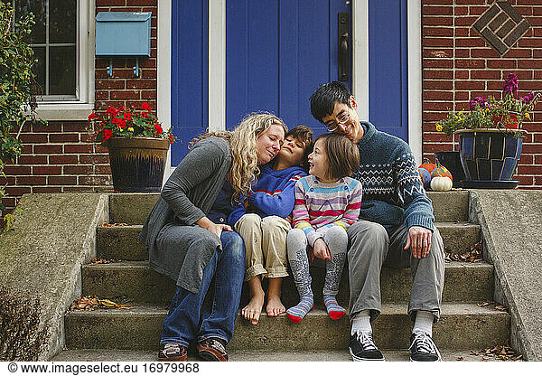 A loving family snuggle together on front stoop of home in autumn
