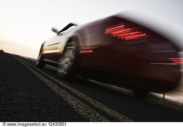 A low angle blurred view of a convertible sports car silhouetted on the road at sunset.