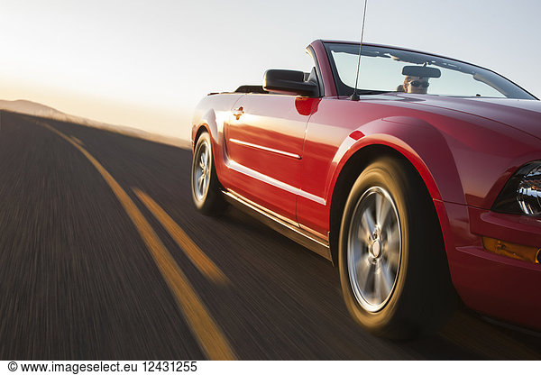A low angle view of a convertible sports car moving on a highway late in the day.