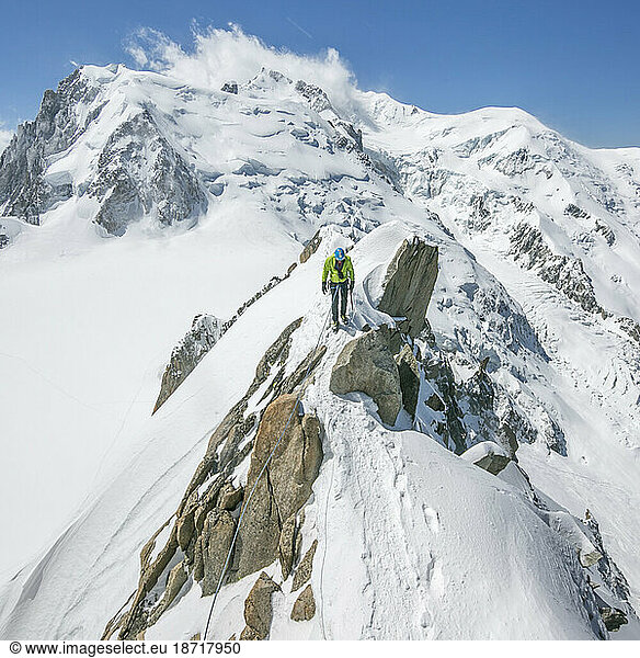 A male alpinist heads across an exposed knife-edge ridge on Mt Blanc