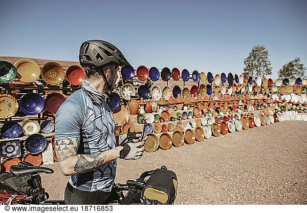 A male cyclist stops next to an outdoor ceramic market  Morocco