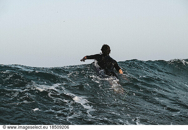 A male surfer paddles on moody sea