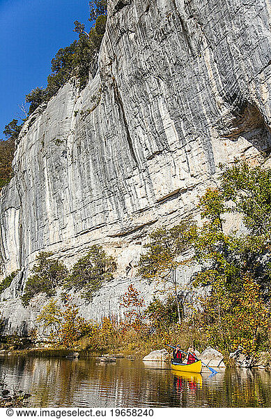 A man and a woman enjoy a calm paddle in a canoe beneath a steep rock wall in Arkansas.
