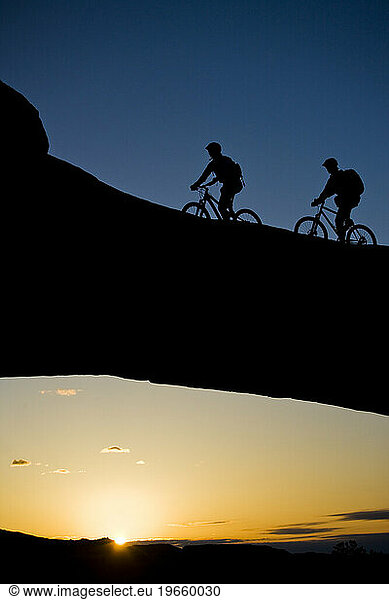 A man and a woman ride across a natural rock arch in the desert near Moab  Utah.