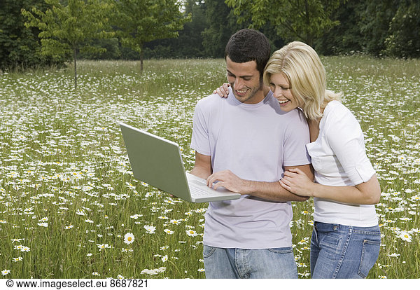 A man and woman in a flower meadow  looking at a laptop screen.