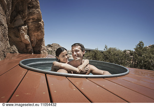 A man and woman on the terrace of an eco home  a low impact house in the desert landscape  in a sunken hot tub.