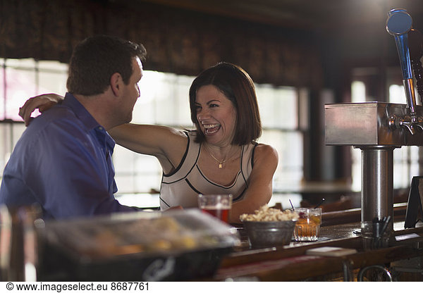 A man and woman seated at a bar  flirting and talking. On a date.