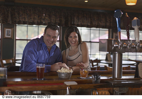 A man and woman side by side seated at a bar  smiling. On a date.