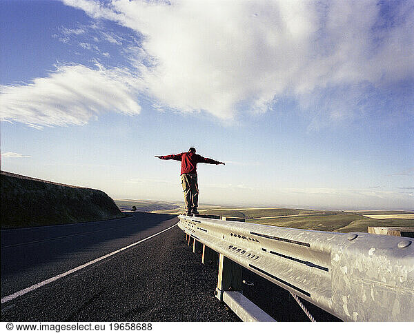 A man balances on the railing near a desolate road in Oregon.