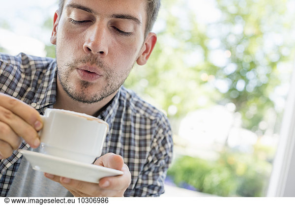 A man blowing on the surface of his hot coffee.