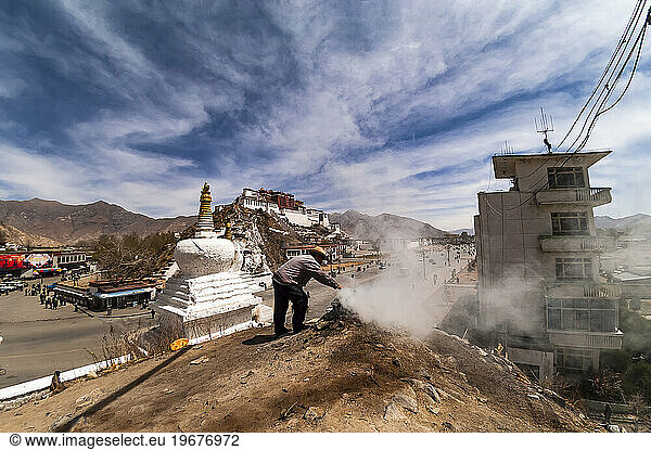 A Man Burning Incense Atop Of A Small Hill With The Potala Palace Behind