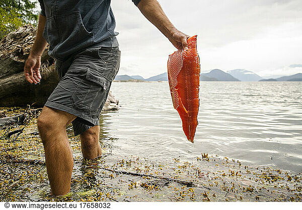 A man carries a fresh salmon filet out of the water