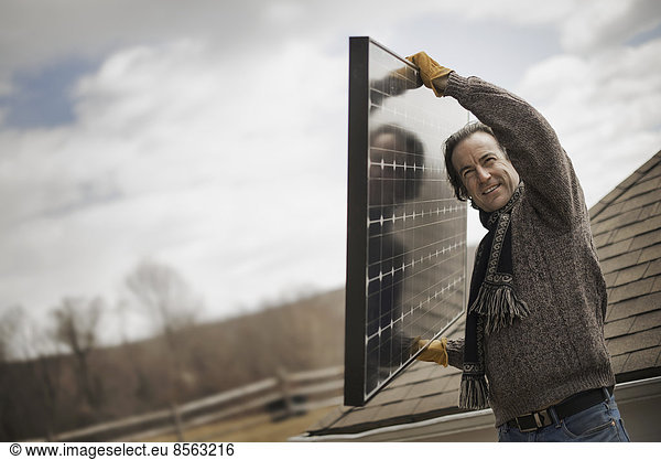 A man carrying a large solar panel across a farmyard.