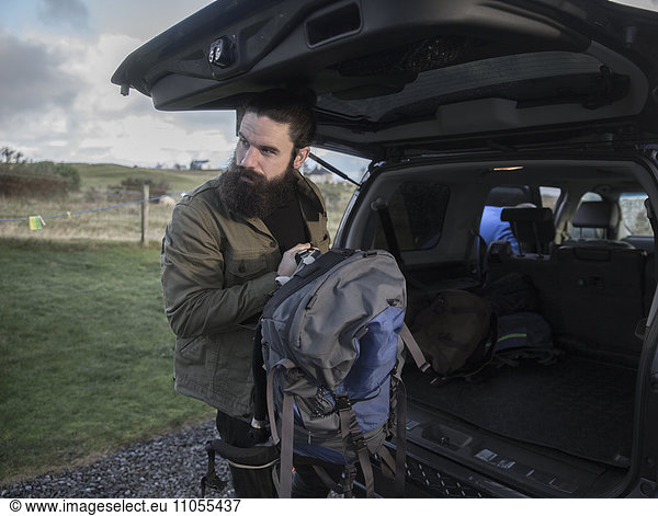 A man carrying a rucksack standing by an open car boot.