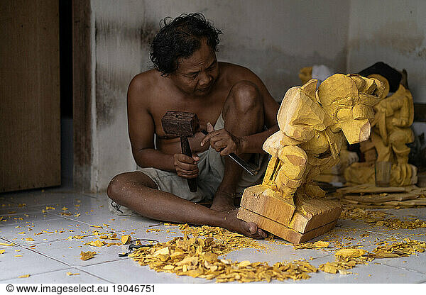 A man carves a statue in wood in workshop. Woodcarving Bali.