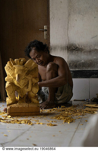 A man carves a statue in wood in workshop. Woodcarving Bali.