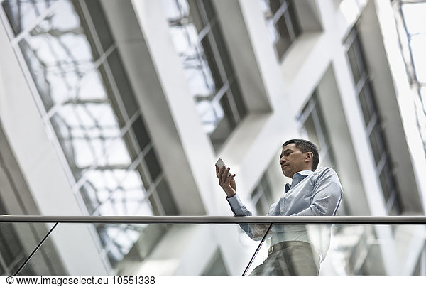 A man checking his smart phone in a large airy building with windows.