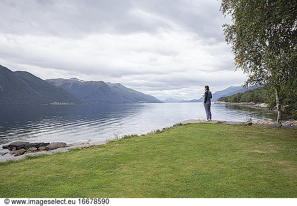 A man drinking a cup of coffee looking across a fjord in Norway