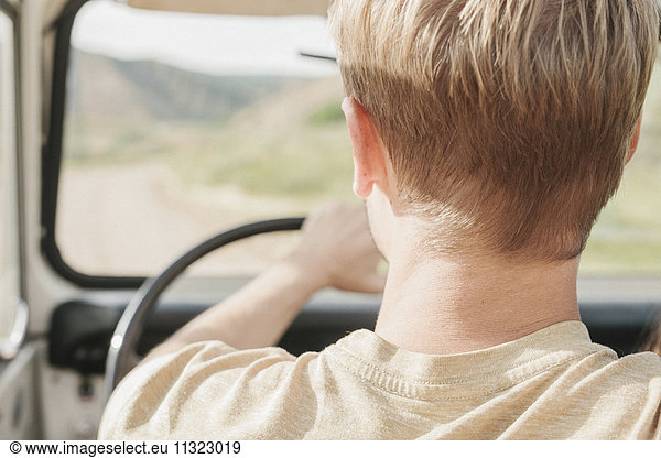 A man driving an open top jeep  rear view.