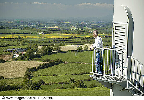 A man examines the view over Collon  Ireland from the steps of a wind turbine.