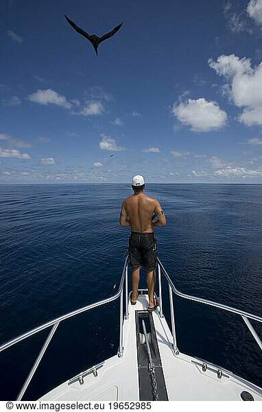 A man fishing off bow of boat as a bird flies through the clouds overhead in the waters off of Costa Rica.
