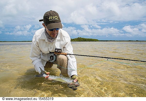 A man fly fisherman holding bonefish fish on the beach in Venezuela Los Roques National Park
