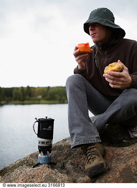 A man having a cup of coffee on a rock by the water Sweden.