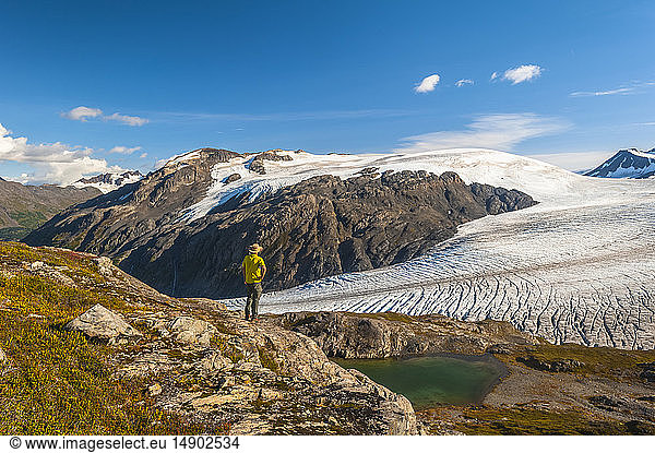 A man hiking near the Harding Icefield Trail with the Kenai Mountains and an unnamed hanging glacier in the background  Kenai Fjords National Park  Kenai Peninsula  South-central Alaska; Alaska  United States of America