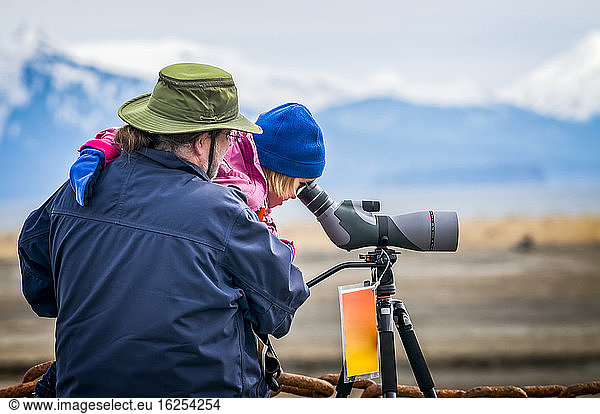 A man holds his daughter to look through a spotting scope during the 21st annual 2013 Kachemak Bay Shorebird Festival. The festival is held in Homer  Alaska  sponsored by the Homer Chamber of Commerce and US Fish & Wildlife Service; Homer  Alaska  United States of America