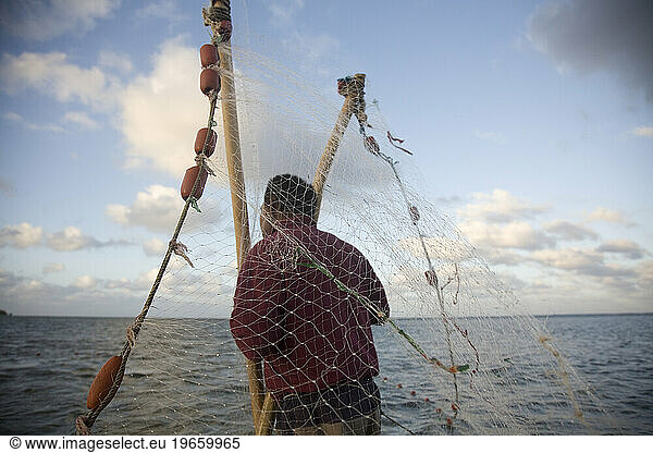A man holds the ends of a net while a woman collects any trapped fish.