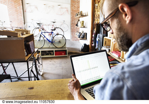 A man in a bicycle repair shop using a laptop computer. Running a business.