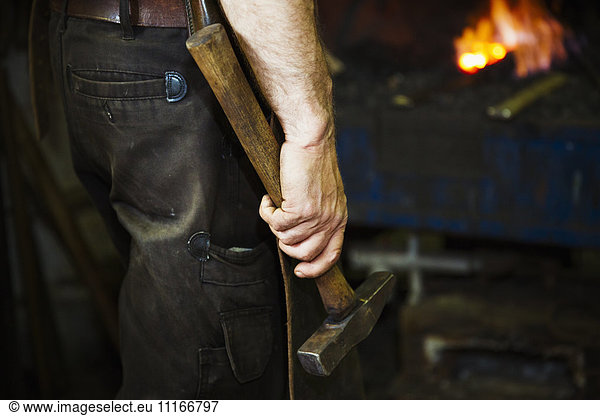 A man in a leather apron holding a hammer in a workshop.