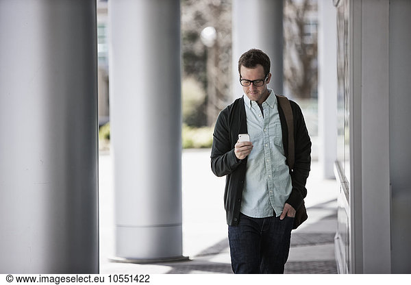 A man in casual clothes standing outside a building  checking his smart phone.