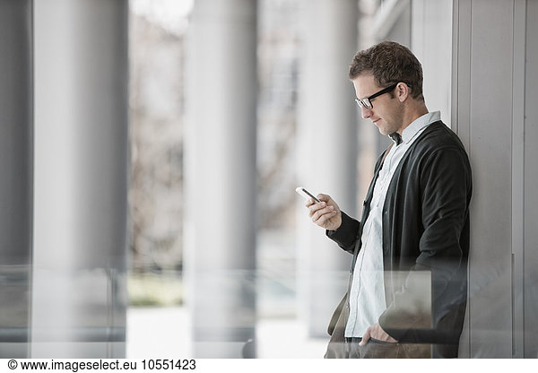 A man in casual clothes standing outside a building  checking his smart phone.