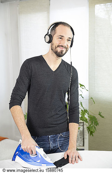 A man ironing while listening to music and smiling.