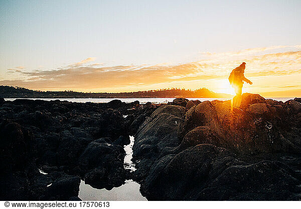 A man is silhouetted while rock hopping over tide pools