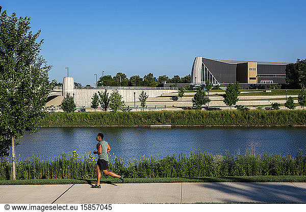 A man jogs along path in a city park against river and tall buildings