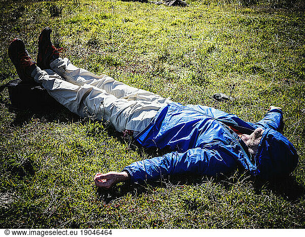 A man laying down on the ground after an exhausing hike.
