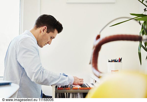 A man looking in a filing cabinet drawing  sorting through hanging files.