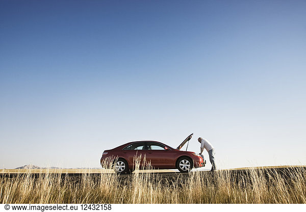 A man looking into the engine compartment of his car parked along a highway in eastern Washington State  USA.