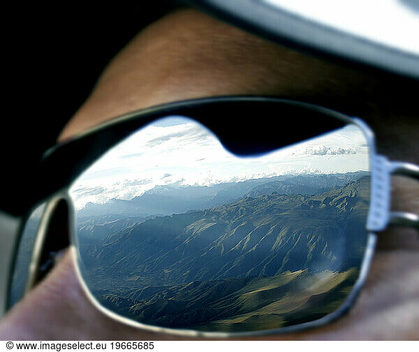 A man looking out to the Andes as his sunglasses catches the reflection of the mountain ranges  Peru.