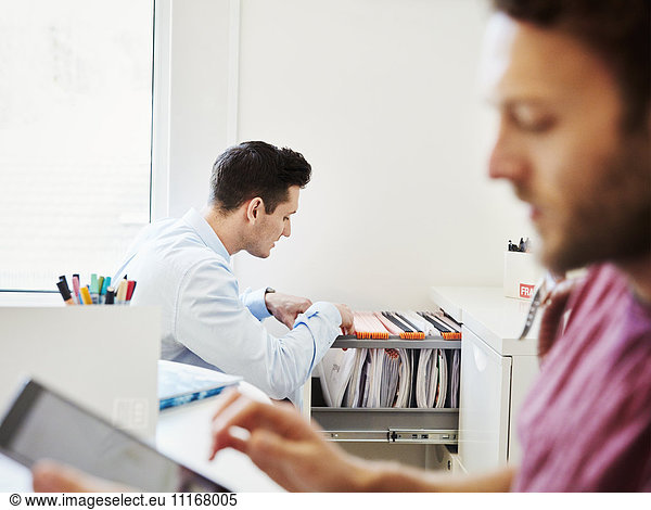A man looking through files in an office  and a man using his digital tablet.