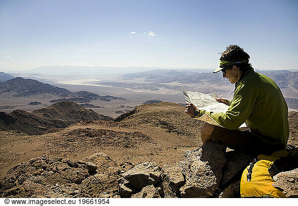 A man looks at a map while sitting on the summit of a peak in Death Valley National Park  California  United States.