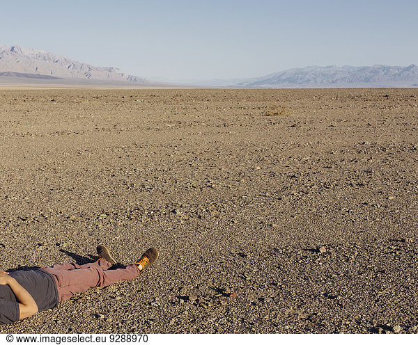 A man lying on his back on the ground in the desert.