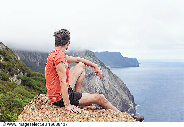 A man on a rock  looking at cliffs and ocean  mountains and fog